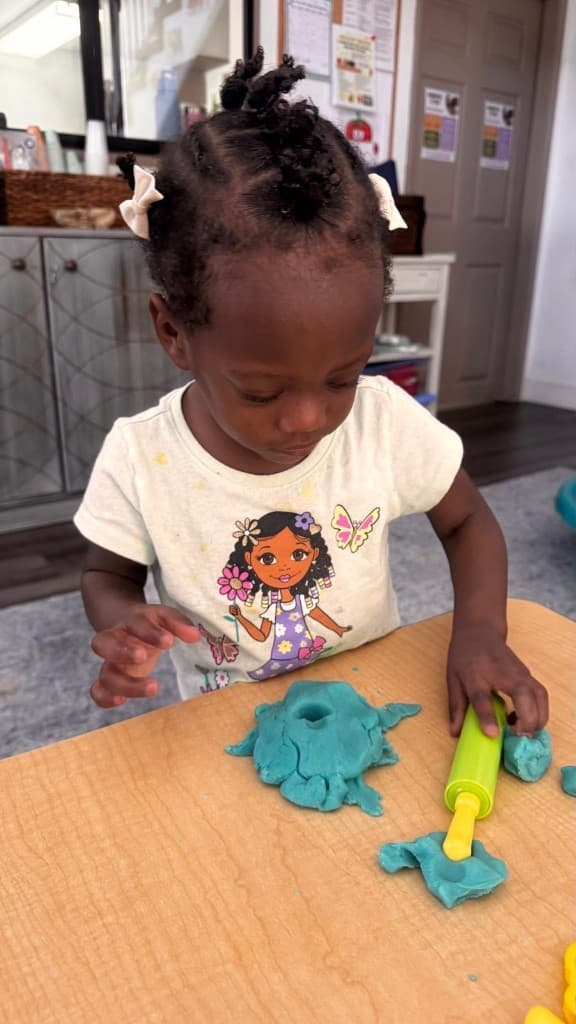 A child rolling blue playdough at a classroom table at Developing Mindful Lives.