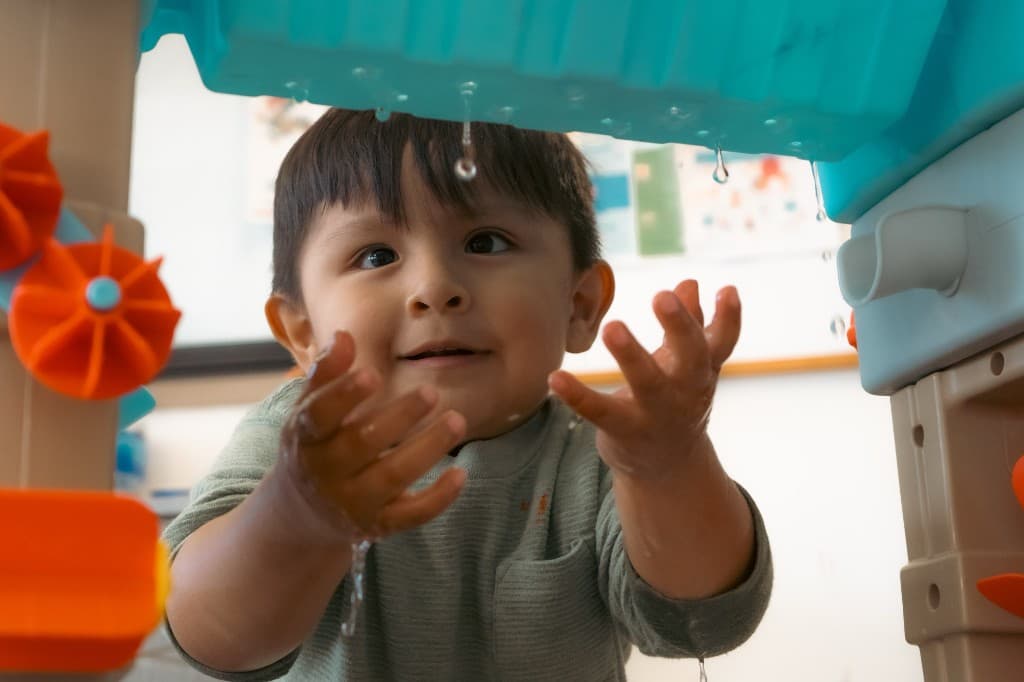 A toddler catching water droplets at a sensory water table at Developing Mindful Lives.
